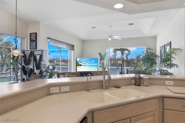 kitchen with light brown cabinetry, sink, hanging light fixtures, ceiling fan, and a raised ceiling