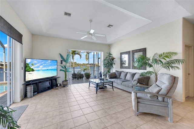 living room with a raised ceiling, ceiling fan, and light tile patterned flooring