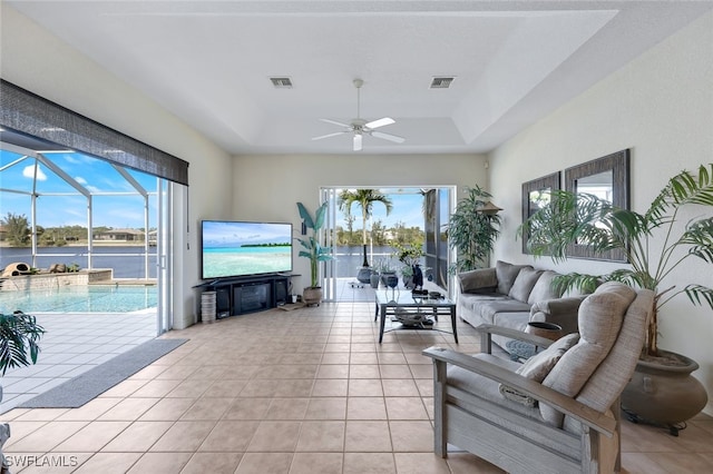 living room with ceiling fan, a raised ceiling, and light tile patterned floors