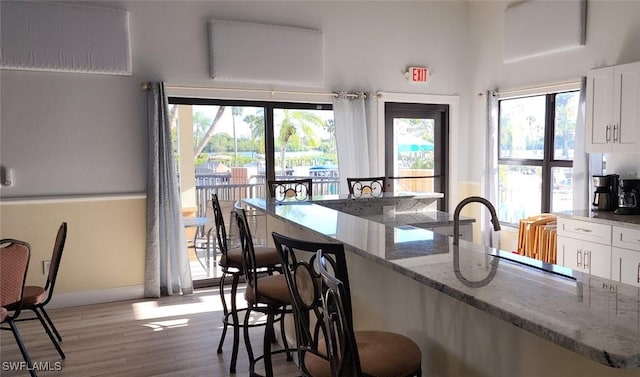 kitchen with white cabinetry, light stone counters, light hardwood / wood-style floors, and a breakfast bar