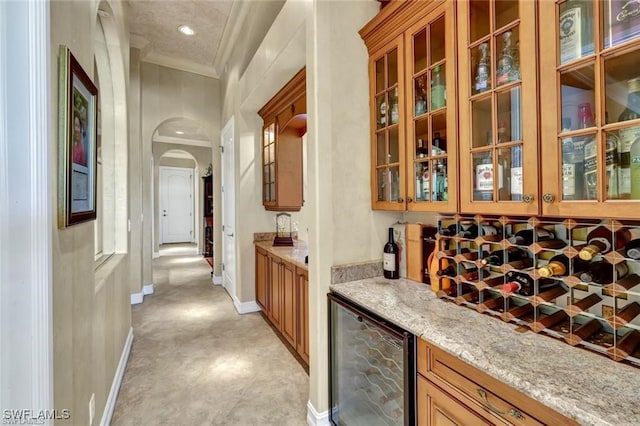 bar with light stone counters, crown molding, and beverage cooler