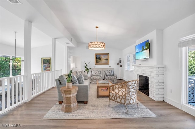 living room with vaulted ceiling, light hardwood / wood-style flooring, and a stone fireplace