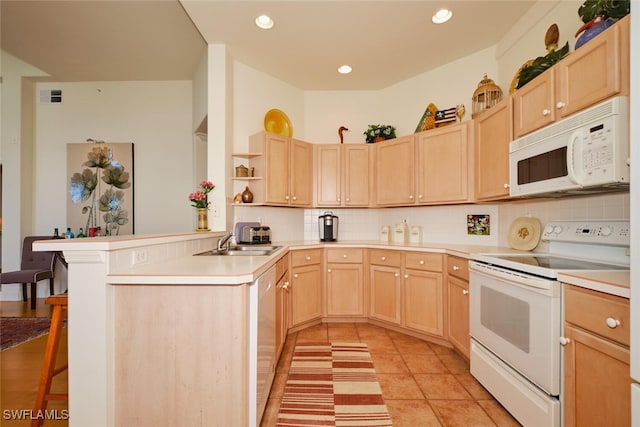 kitchen featuring kitchen peninsula, light brown cabinetry, decorative backsplash, a kitchen bar, and white appliances