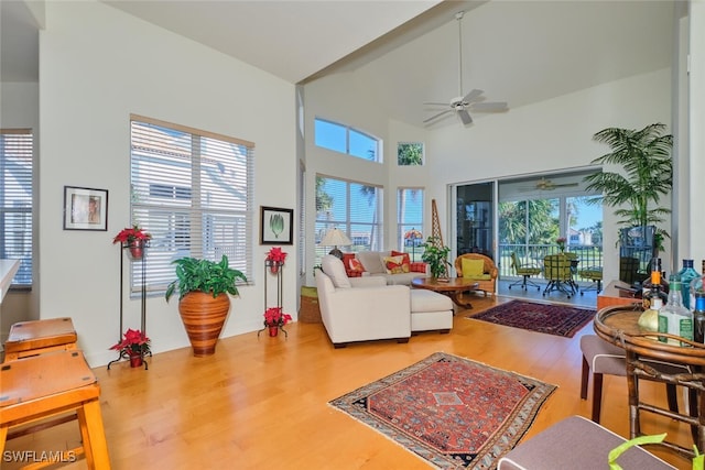 living room with a wealth of natural light, ceiling fan, wood-type flooring, and a high ceiling