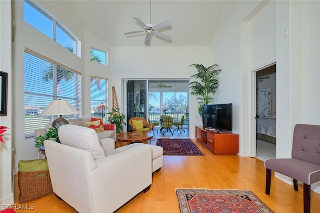 living room with a towering ceiling, light hardwood / wood-style flooring, and ceiling fan