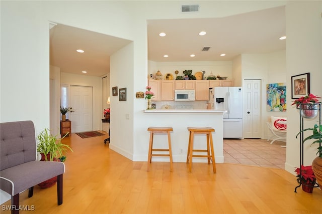 kitchen featuring a kitchen breakfast bar, kitchen peninsula, light hardwood / wood-style floors, white appliances, and light brown cabinetry