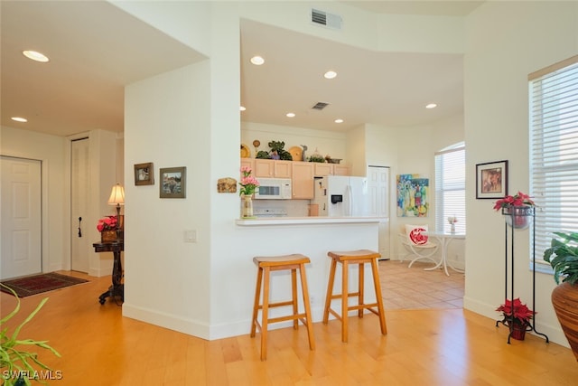 kitchen featuring kitchen peninsula, white appliances, a breakfast bar area, light brown cabinetry, and light wood-type flooring