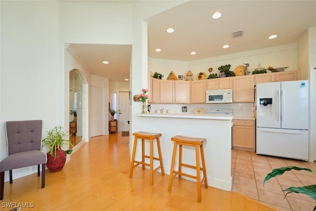 kitchen with light brown cabinets, white appliances, a kitchen breakfast bar, tasteful backsplash, and kitchen peninsula