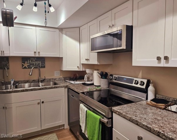 kitchen featuring light stone counters, stainless steel appliances, white cabinetry, and sink