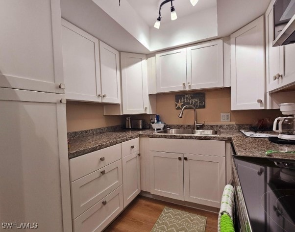 kitchen featuring sink, rail lighting, light hardwood / wood-style flooring, dark stone countertops, and white cabinets