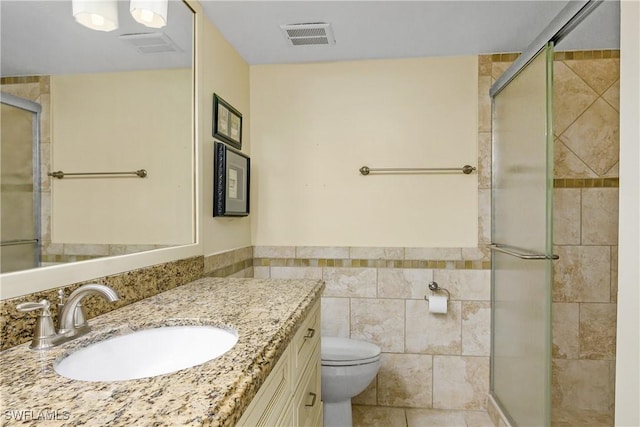 bathroom featuring toilet, a shower with shower door, tile patterned flooring, tile walls, and vanity