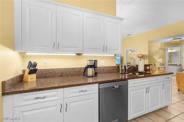 kitchen with light tile patterned floors, dark stone counters, white cabinets, stainless steel dishwasher, and a sink