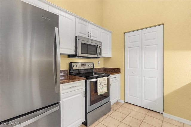 kitchen featuring light tile patterned floors, stainless steel appliances, baseboards, white cabinets, and dark stone countertops