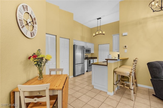 kitchen featuring stainless steel appliances, a chandelier, a high ceiling, light tile patterned flooring, and a peninsula