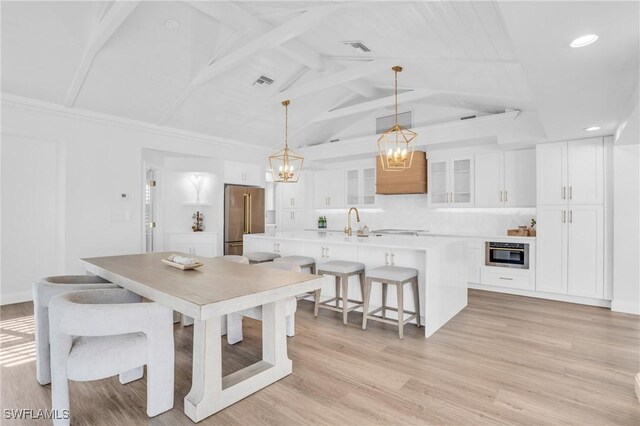 dining space with sink, lofted ceiling with beams, light hardwood / wood-style flooring, and a notable chandelier