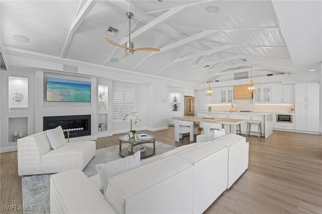 living room featuring lofted ceiling with beams, sink, ceiling fan with notable chandelier, and light hardwood / wood-style floors