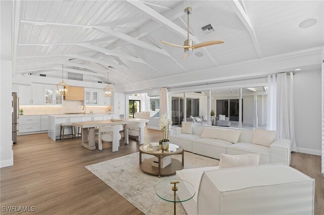 living room featuring ceiling fan, vaulted ceiling with beams, sink, and light wood-type flooring