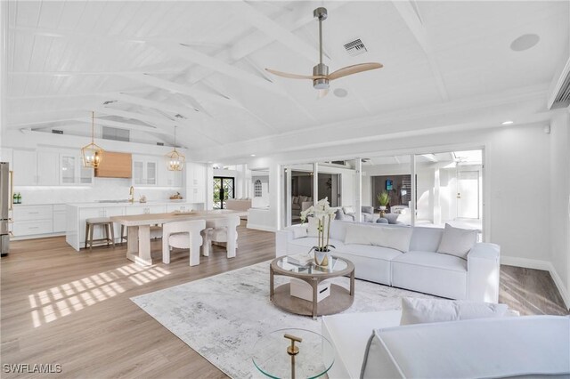 living room featuring ceiling fan, sink, lofted ceiling with beams, and light wood-type flooring