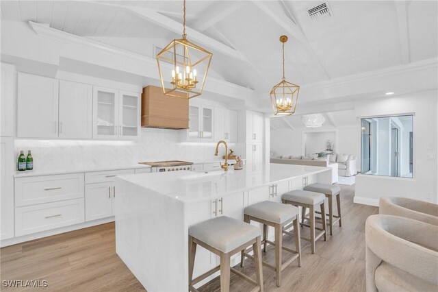 kitchen featuring a breakfast bar, decorative light fixtures, an island with sink, white cabinets, and backsplash