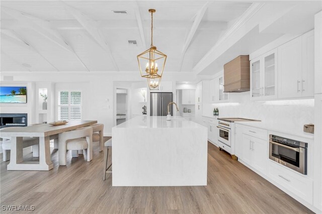 kitchen featuring white cabinetry, hanging light fixtures, stainless steel appliances, and a center island with sink