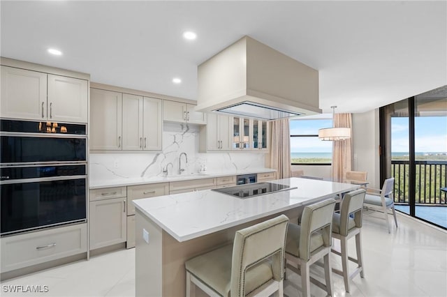 kitchen with light stone countertops, sink, hanging light fixtures, premium range hood, and black appliances