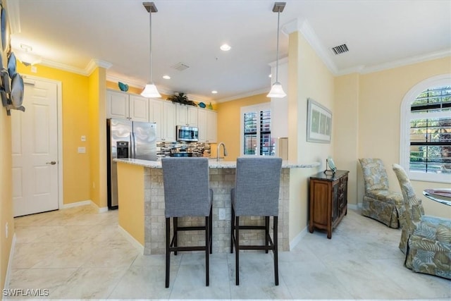 kitchen featuring appliances with stainless steel finishes, hanging light fixtures, ornamental molding, a breakfast bar, and light stone counters