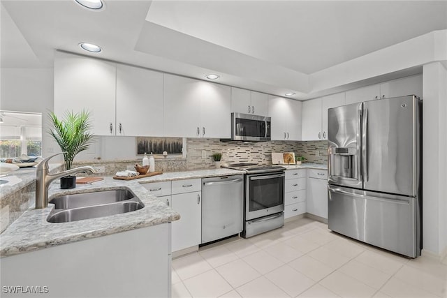 kitchen with light stone countertops, sink, backsplash, white cabinets, and appliances with stainless steel finishes