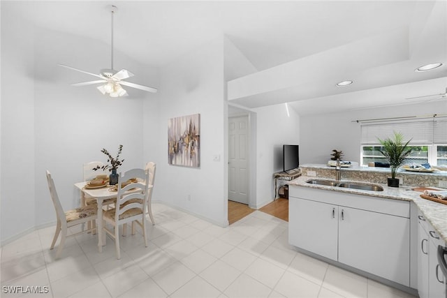 kitchen with lofted ceiling, white cabinets, sink, ceiling fan, and light stone countertops