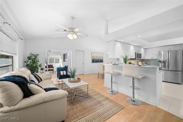 living room featuring ceiling fan, a healthy amount of sunlight, vaulted ceiling, and light wood-type flooring