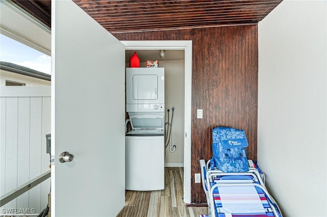 laundry area featuring light wood-type flooring, stacked washer / dryer, wood walls, and wood ceiling