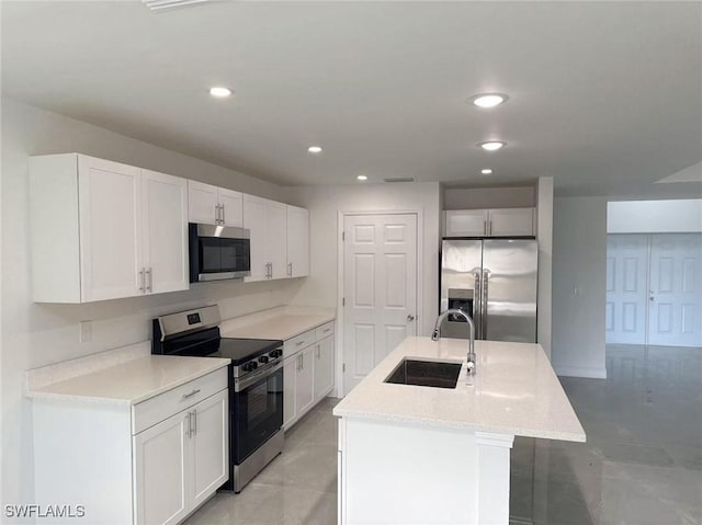 kitchen with a center island with sink, sink, light stone countertops, appliances with stainless steel finishes, and white cabinetry