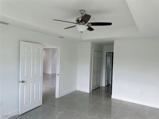 empty room featuring ceiling fan and a tray ceiling