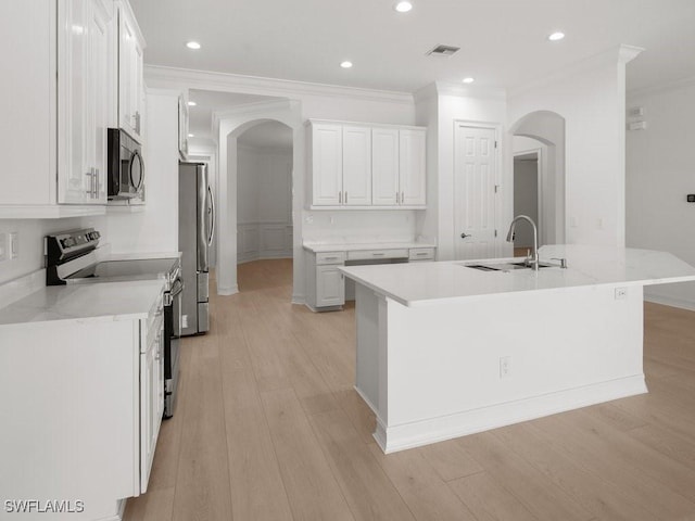 kitchen with appliances with stainless steel finishes, a kitchen island with sink, light stone countertops, white cabinets, and light wood-type flooring