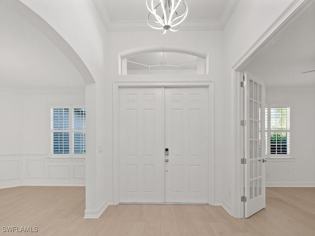 foyer entrance with crown molding, an inviting chandelier, and light wood-type flooring