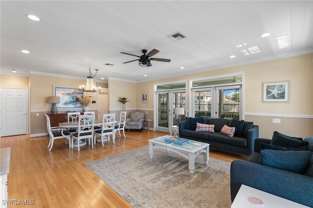 living room with ceiling fan with notable chandelier, ornamental molding, and light hardwood / wood-style flooring