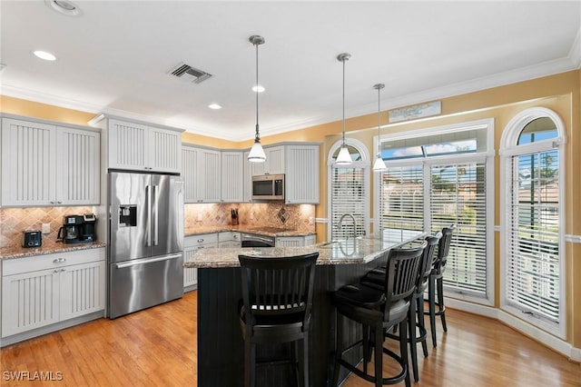 kitchen with a kitchen island with sink, light stone countertops, pendant lighting, and appliances with stainless steel finishes