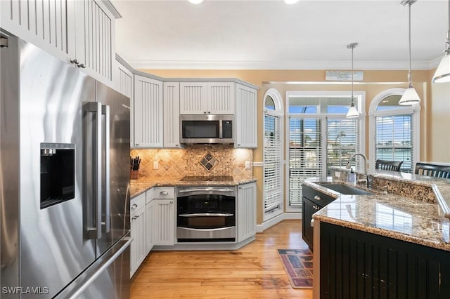 kitchen with sink, stainless steel appliances, backsplash, light hardwood / wood-style floors, and decorative light fixtures