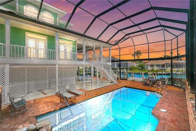 pool at dusk with a lanai, a patio area, and a water view