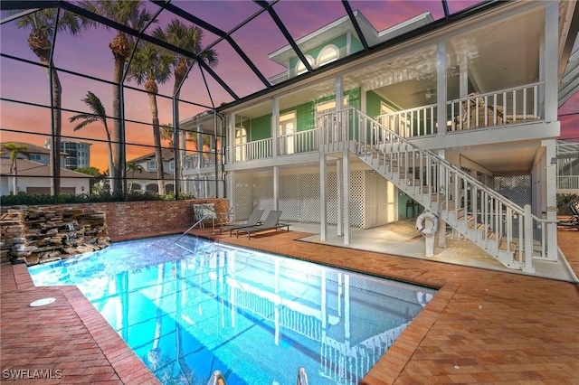 pool at dusk with glass enclosure and a patio area