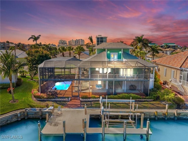 back house at dusk featuring a water view, a lanai, a balcony, a yard, and a patio area