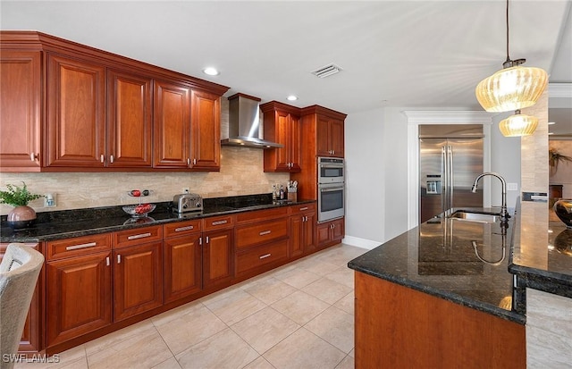 kitchen featuring sink, dark stone counters, hanging light fixtures, stainless steel appliances, and wall chimney exhaust hood