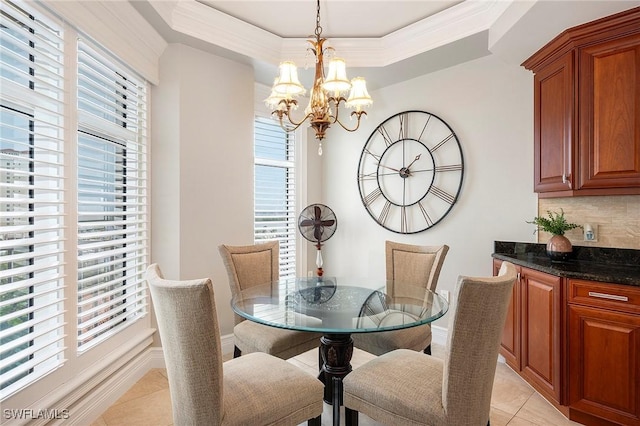 dining space featuring light tile patterned flooring, a notable chandelier, baseboards, a tray ceiling, and crown molding