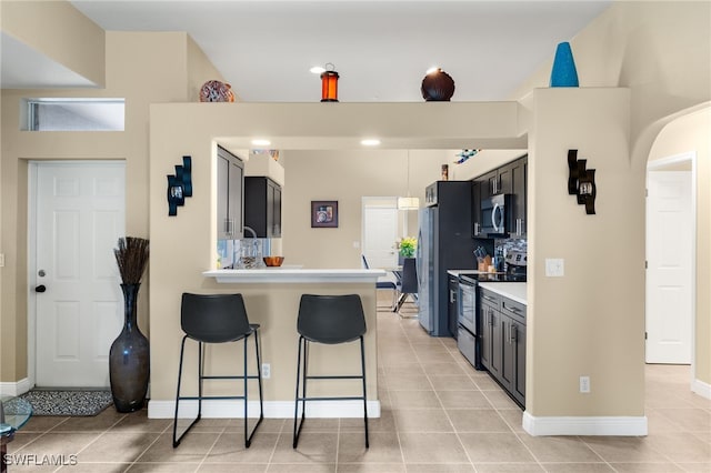 kitchen with stainless steel appliances, kitchen peninsula, a breakfast bar area, decorative backsplash, and light tile patterned flooring