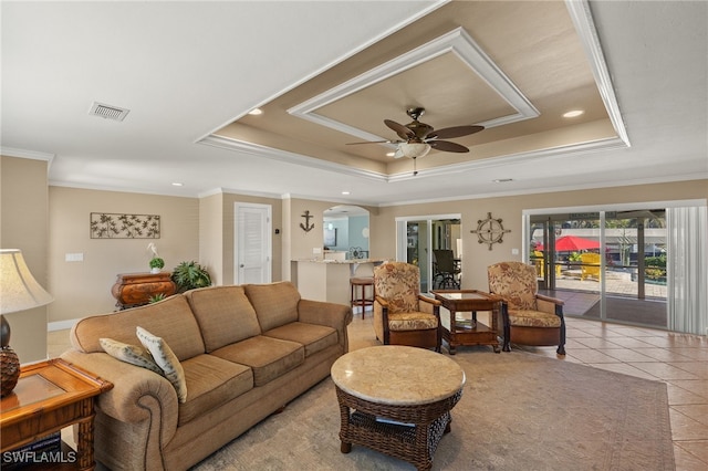 living room with crown molding, ceiling fan, a tray ceiling, and light tile patterned floors