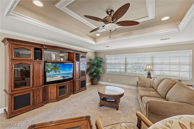 living room with ceiling fan, ornamental molding, a tray ceiling, and light tile patterned floors