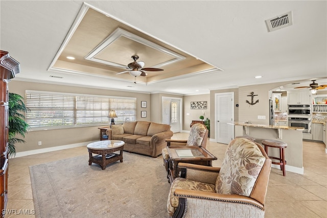 living room featuring ornamental molding, light tile patterned floors, ceiling fan, and a tray ceiling