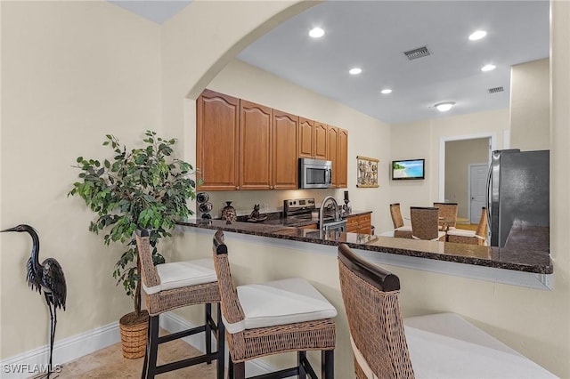 kitchen with kitchen peninsula, stainless steel appliances, sink, dark stone countertops, and a breakfast bar area