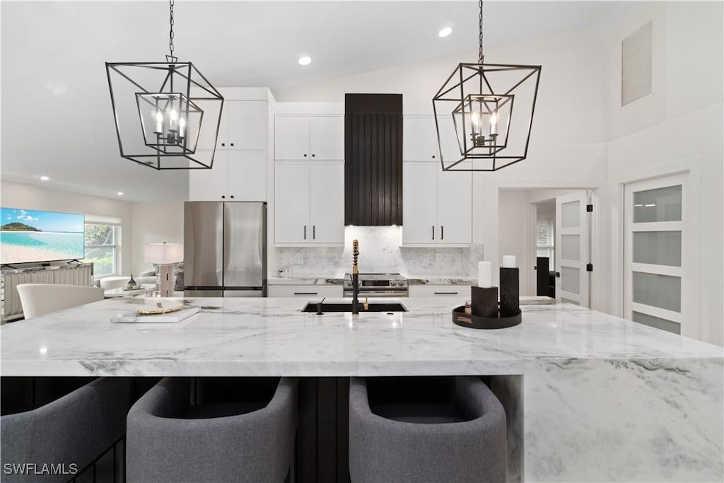 kitchen featuring vaulted ceiling, range hood, pendant lighting, sink, and stainless steel fridge