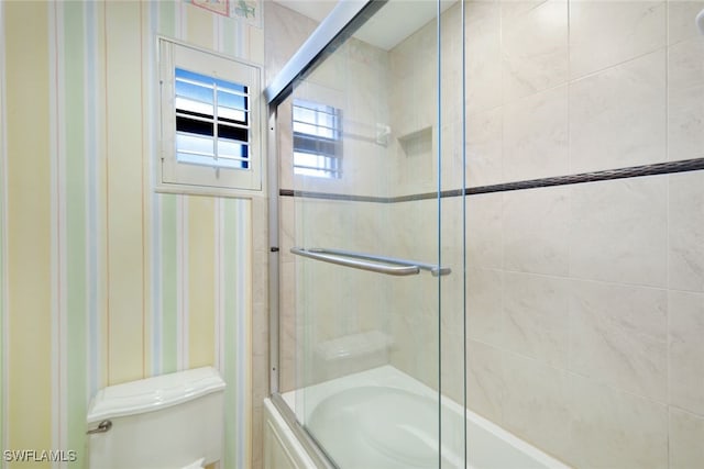 bathroom with toilet and shower / bath combination with glass door