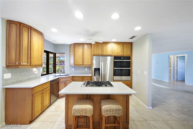 kitchen with ceiling fan, sink, stainless steel appliances, a kitchen bar, and a kitchen island